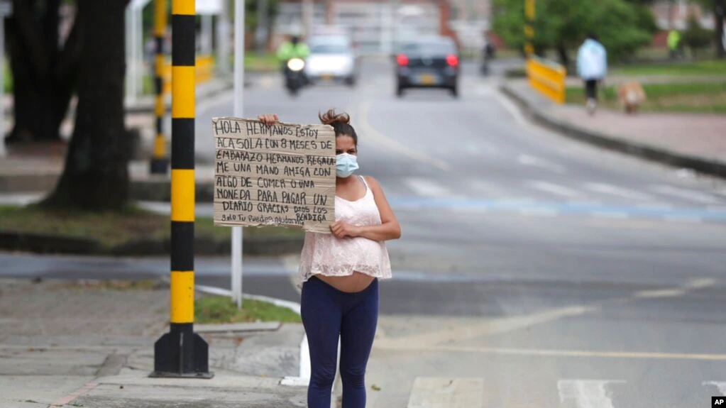 Migrante venezolana sostiene un cartel con un mensaje escrito a mano pidiendo comida o dinero en un cruce peatonal en Bogotá, Colombia, el 9 de febrero de 2021.