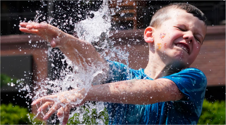 Un niño se refresca en una fuente afuera del Wrigley Field antes de un partido de béisbol entre los Chicago Cubs y los St. Louis Cardinals mientras el clima cálido desciende sobre el área de Chicago el domingo 16 de junio de 2024. (Foto AP/Nam Y. Huh)