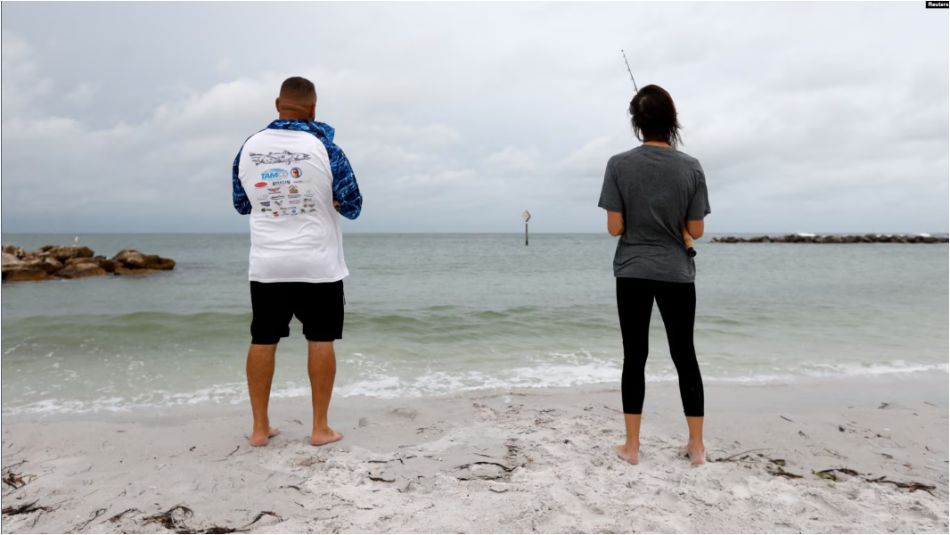 Dos personas pescan durante un clima nublado en la playa de Saint Pete, Florida, el domingo 4 de agosto de 2024.