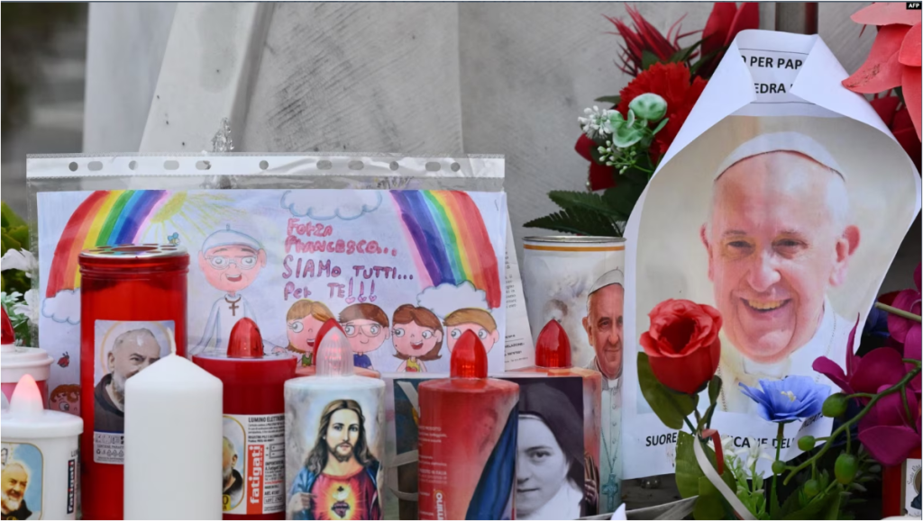 Velas, flores y un retrato del Papa Francisco se colocan en la estatua de Juan Pablo II afuera del hospital Gemelli, donde está hospitalizado el Papa Francisco, en Roma, el 24 de febrero de 2025.